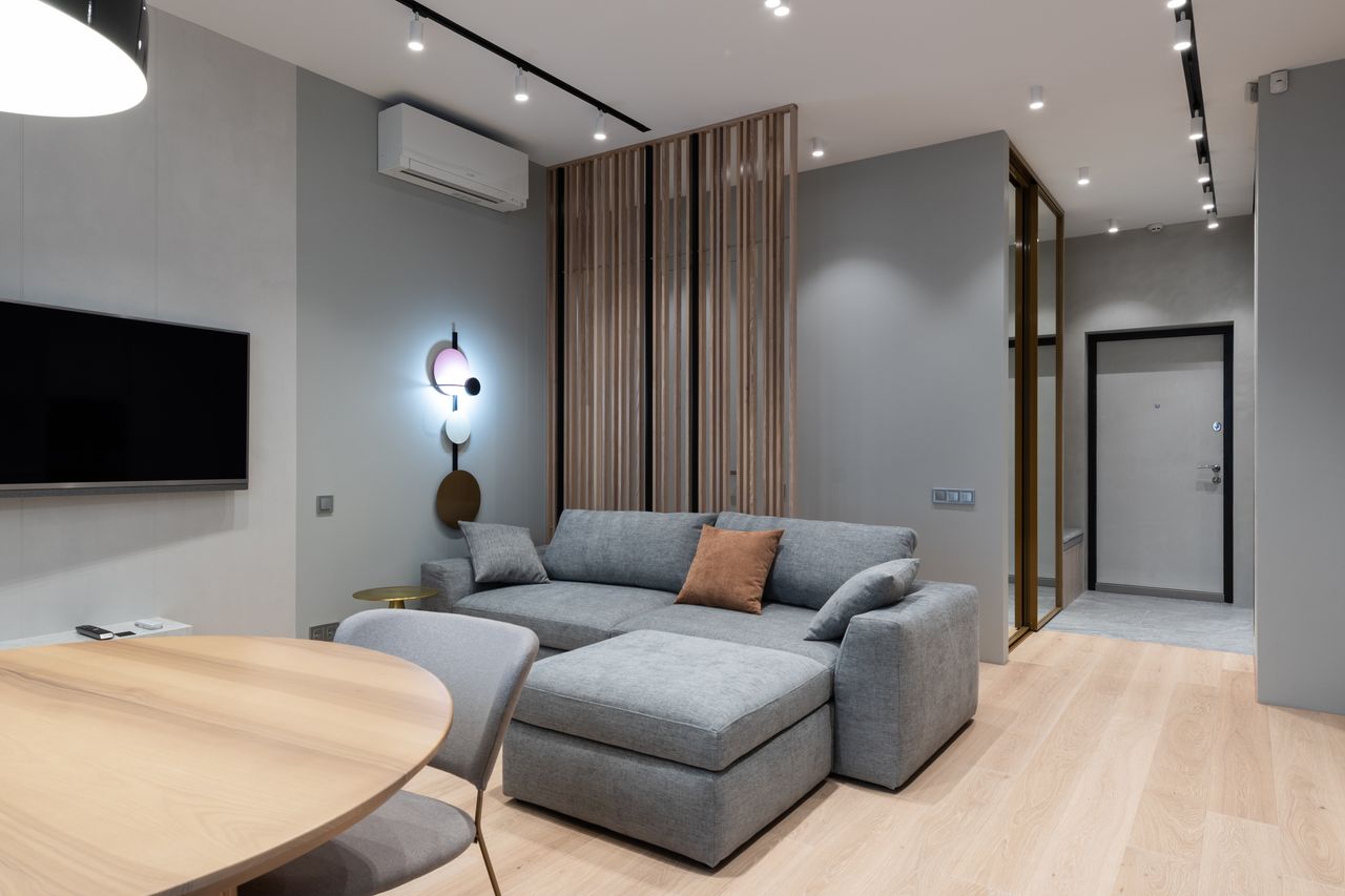 Interior of modern living room with comfortable gray sofa soft cushions and wooden table placed near wall with TV and air conditioner